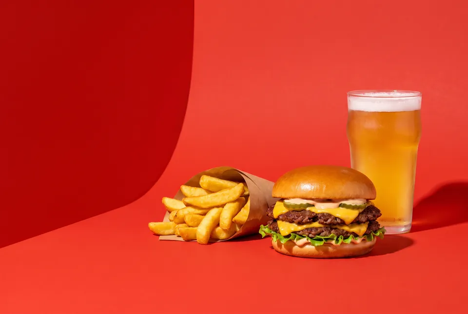 Una hamburguesa doble, unas patatas Gorrón y una cerveza sobre papel rojo